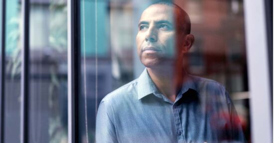 Mature businessman looking through window. Thoughtful male professional is seen through glass at creative office. He is wearing shirt.